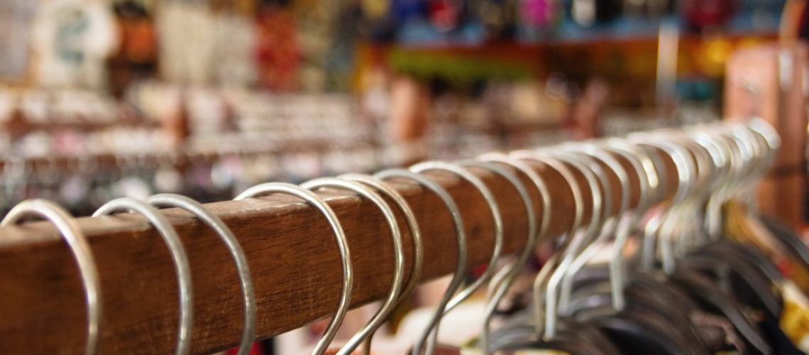 wooden-clothes-racks-with-hangers-and-with-colorful-clothes-on-a-blurred-background-inside-a-shop_t20_lorNGb